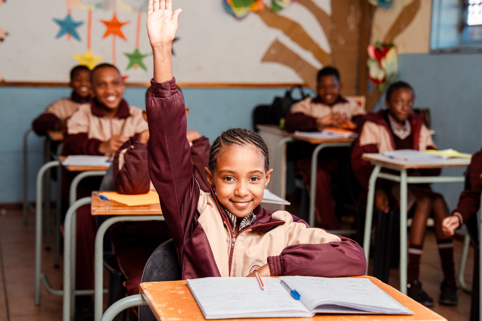 A pupil smiles while raising her hand in class