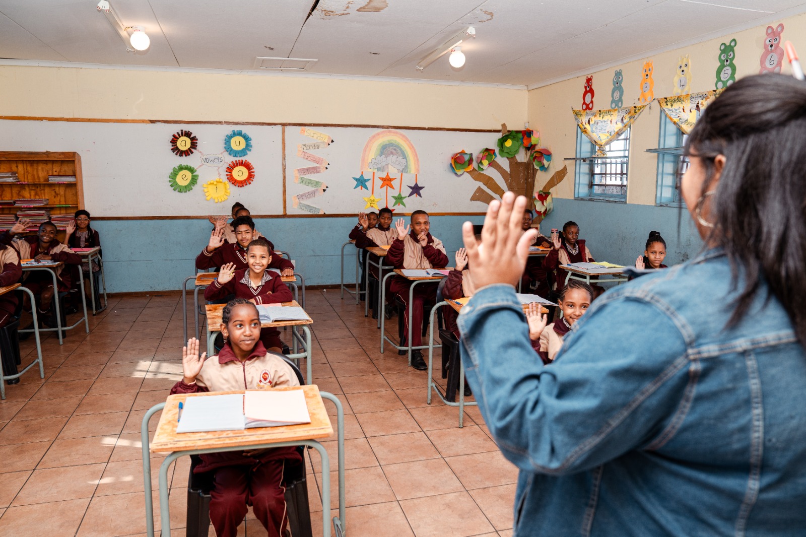 A primary classroom raises their hands together